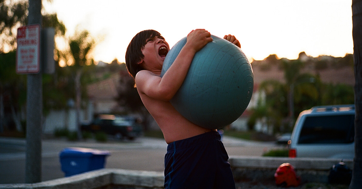Boy struggling to lif a heavy blue exercise ball as a metaphor for inventory management batch operations.