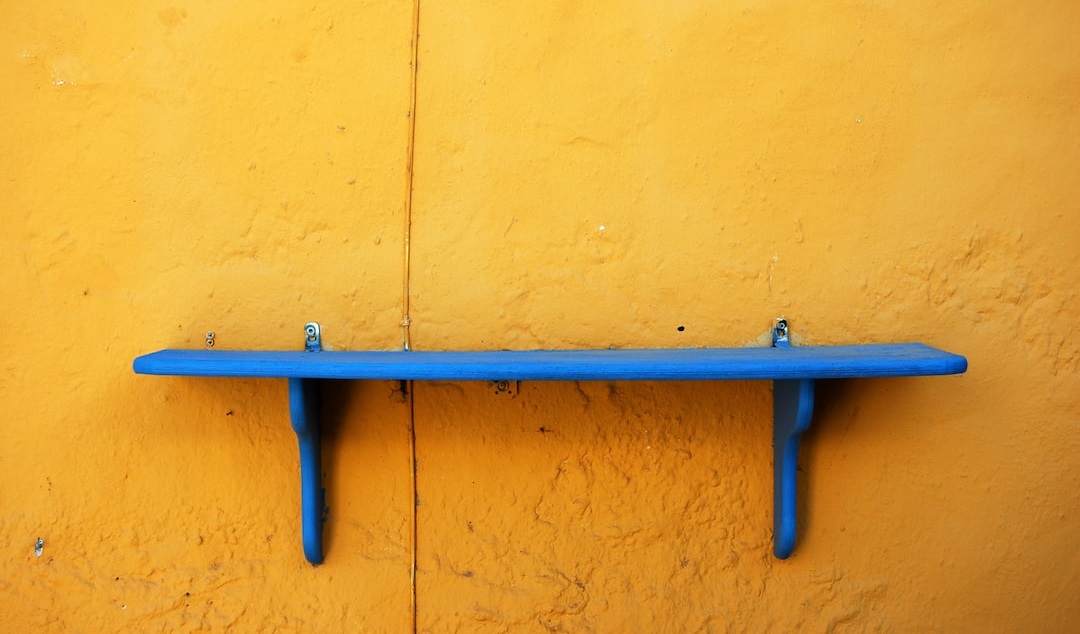 A bright blue wooden shelf on a yellow wall. A metaphor for empty inventory shelves.